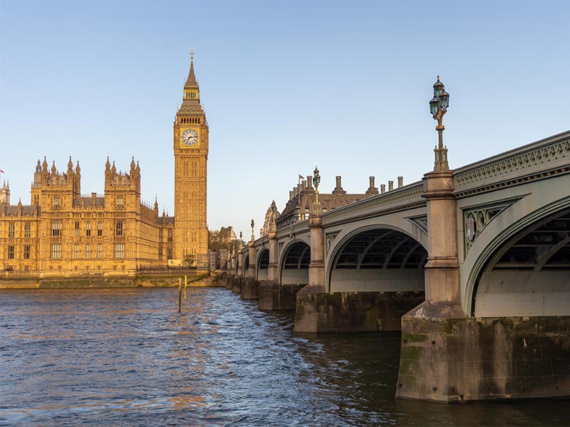 The Houses of Parliament and Big Ben (Elizabeth Tower) stand illuminated by golden hour light, overlooking the River Thames and Westminster Bridge in London, England.