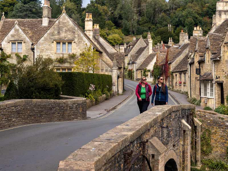 Two women walk across the bridge in Castle Combe