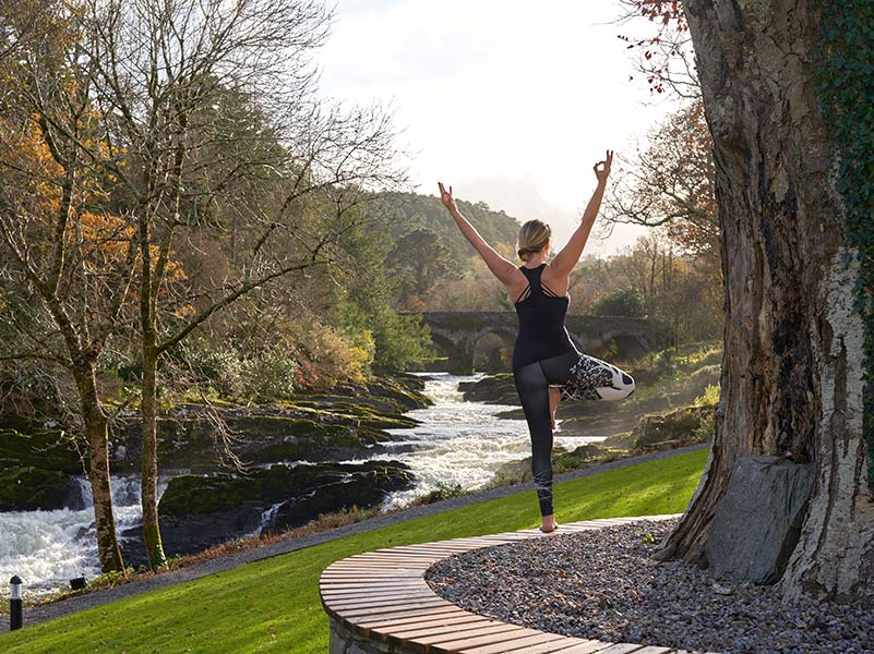 Lady doing a yoga pose against the background of Sheen Falls